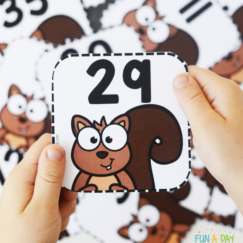 child's hand holding squirrel number card 29 over pile of calendar numbers
