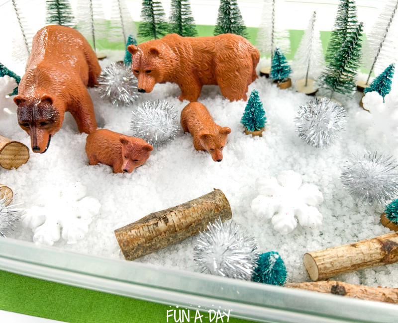 small sensory bin with toy bears, trees, pompoms, snowflakes and fake snow