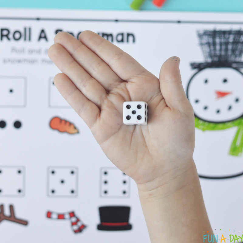 child's hand holding a die over completed roll a snowman printable