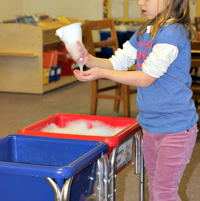 preschooler using funnel in soapy spring water sensory bin