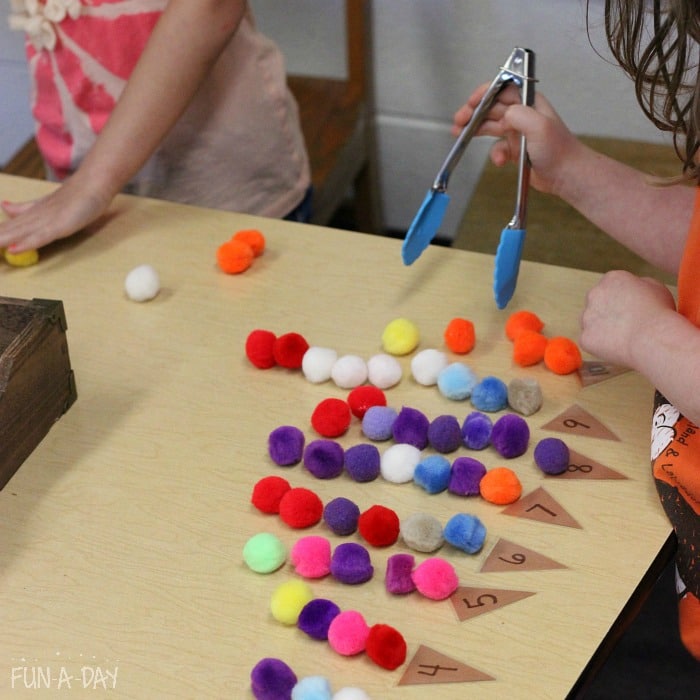 preschoolers using tongs to move and count pompoms on top of numbered cones