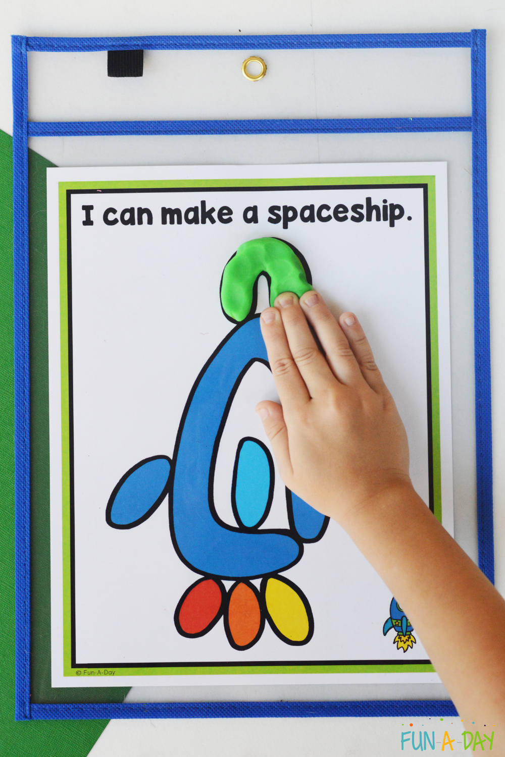 child adding green dough to a space playdough mat with text that reads I can make a spaceship.