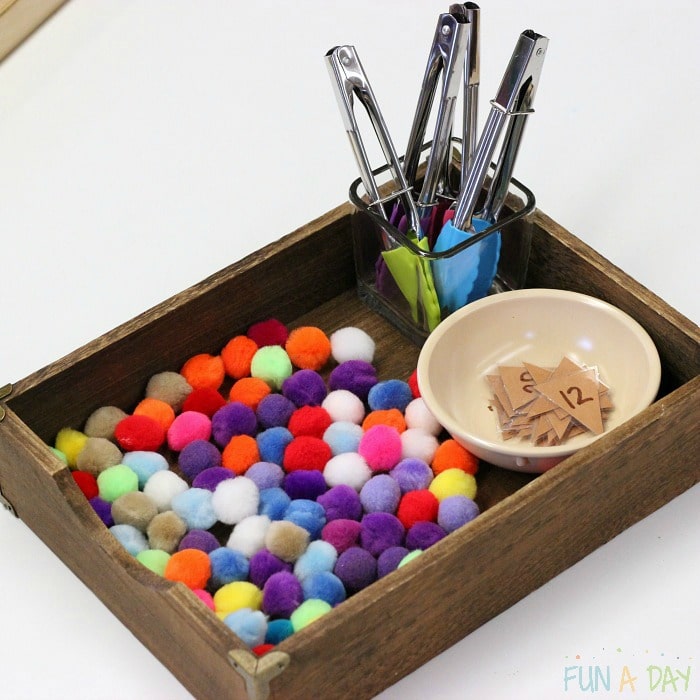 wooden tray with colorful pompoms, kid-sized tongs, and numbered triangles for preschool ice cream math activity