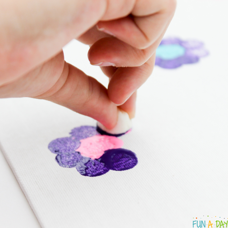 close up of child using a mini marshmallow to paint a purple flower