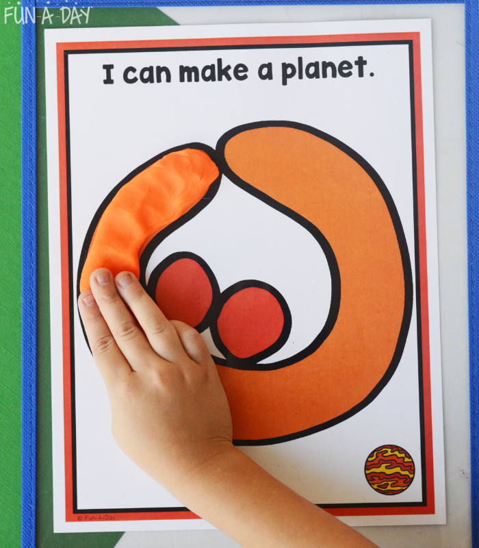 preschooler adding orange dough to a planet play dough mat