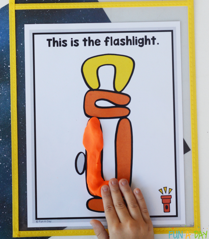 child adding orange dough to a camping play dough mat that reads this is the flashlight