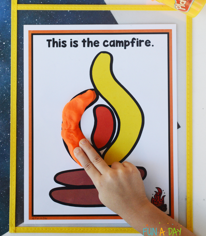preschooler putting orange dough on a camping playdough mat that reads this is the campfire