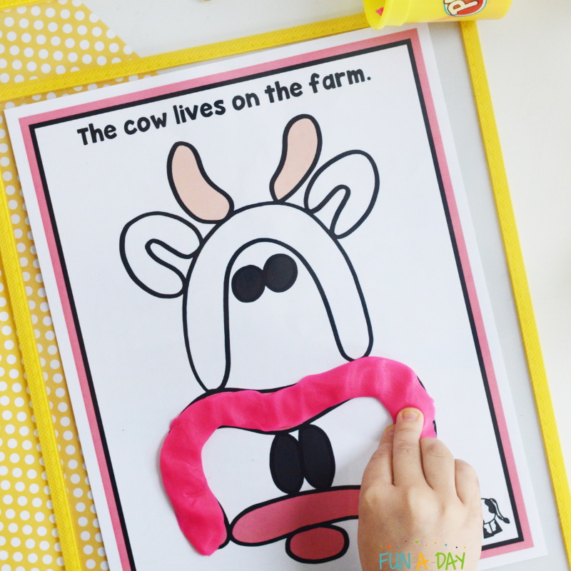 child putting pink dough on a farm animal play dough mat picturing a cow