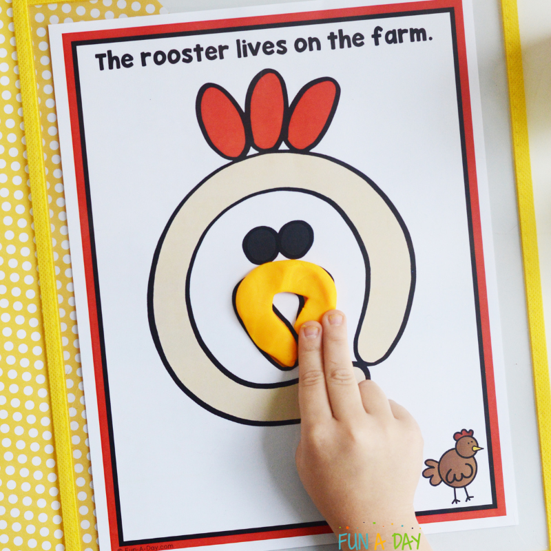 preschooler using one of the farm animal playdough mats that reads the rooster lives on the farm