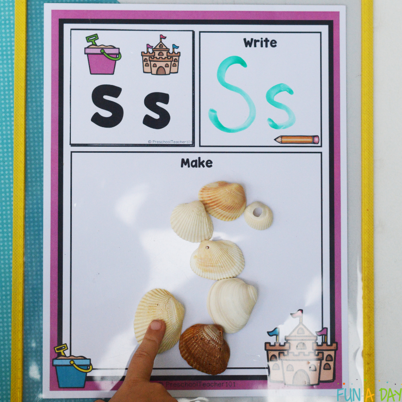 child using shells to make letter S on summer alphabet building mat