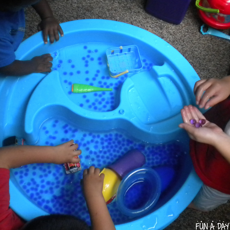 children playing in a round sensory table filled with water and water beads