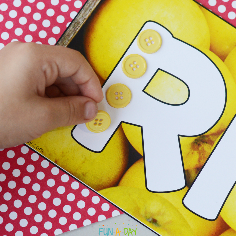 preschooler adding yellow buttons to letter R apple ABC mat