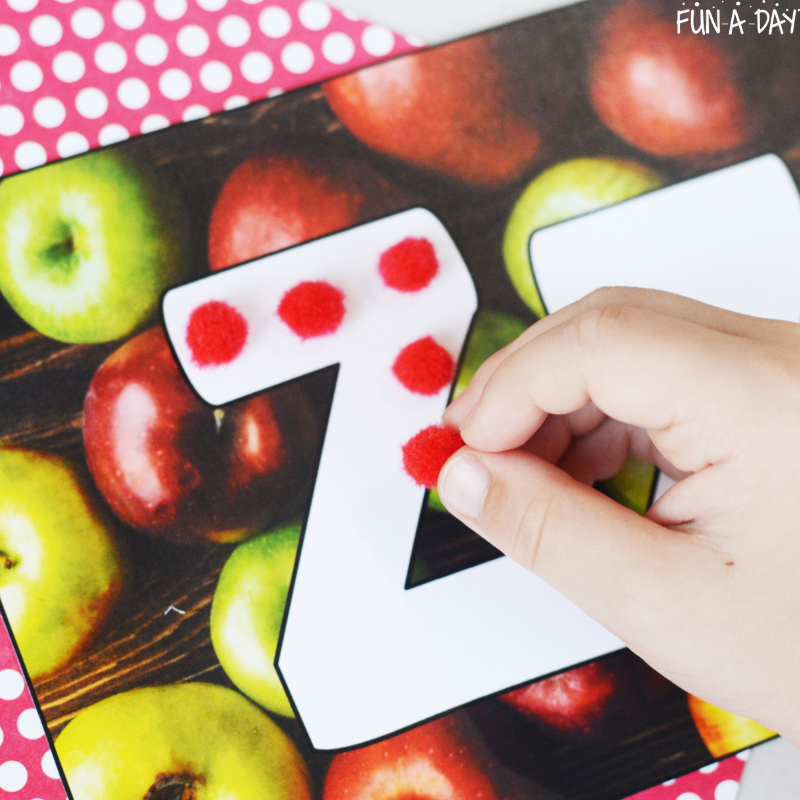 child using red pompoms to trace the letter z on apple ABC mat