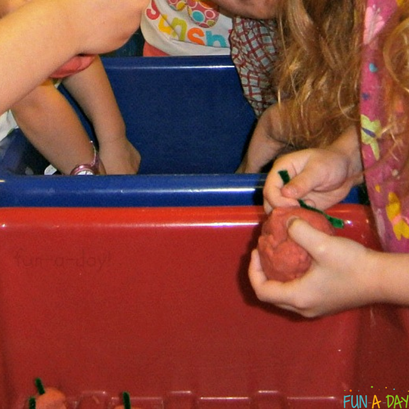 preschoolers using apple pie playdough and chenille stems to make apples in a sensory bin