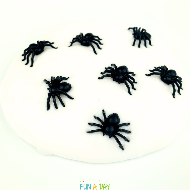 pile of white slime with 7 black toy spiders in it to make spider slime