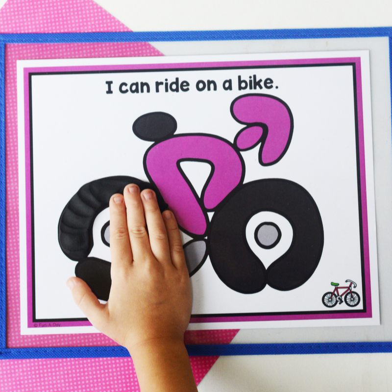 child adding black play dough to transportation playdough mat that reads I can ride on a bike.