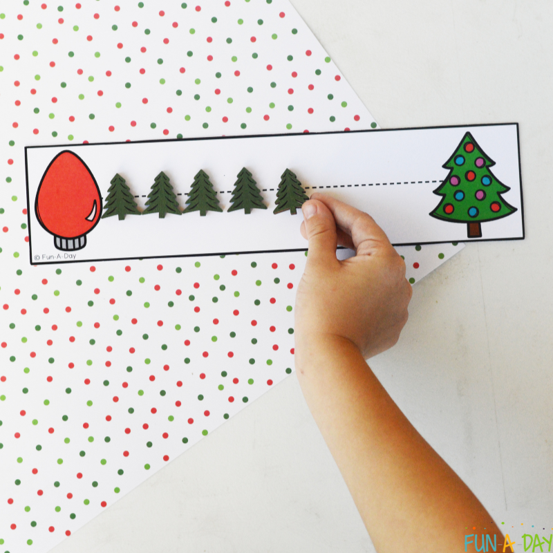 preschooler placing tree loose parts on dotted line along christmas tracing printable