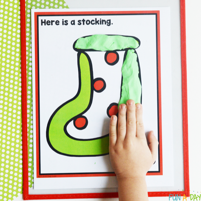 preschooler adding green play dough to make a stocking on one of the christmas playdough mats