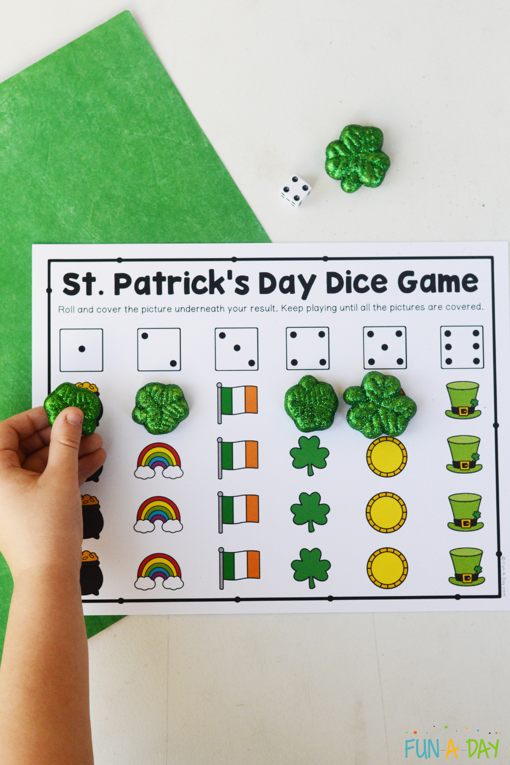 child placing a shamrock manipulative on st. patrick's day dice game printable, under the picture of a die