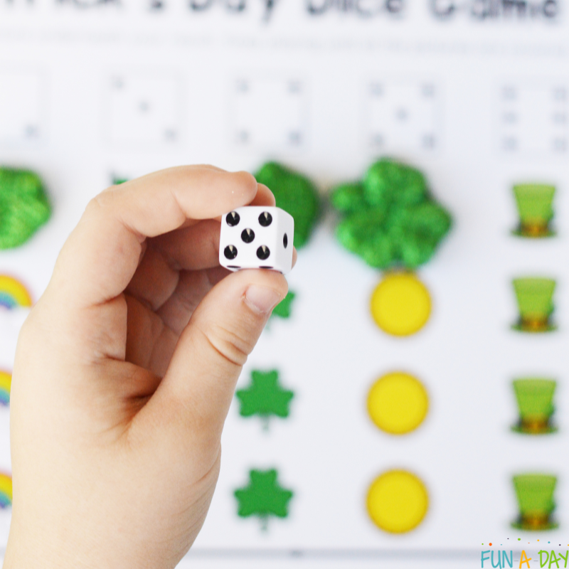preschooler holding a die above printable st. patrick's day number game