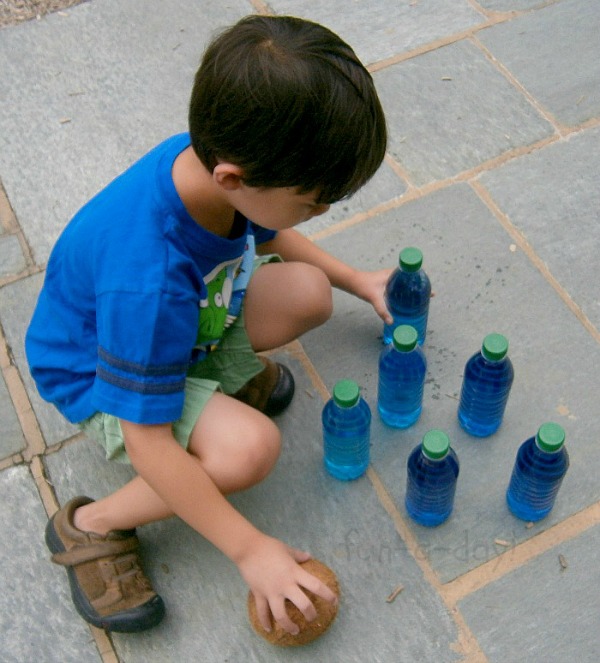 child setting up items for coconut bowling game outside during summer camp