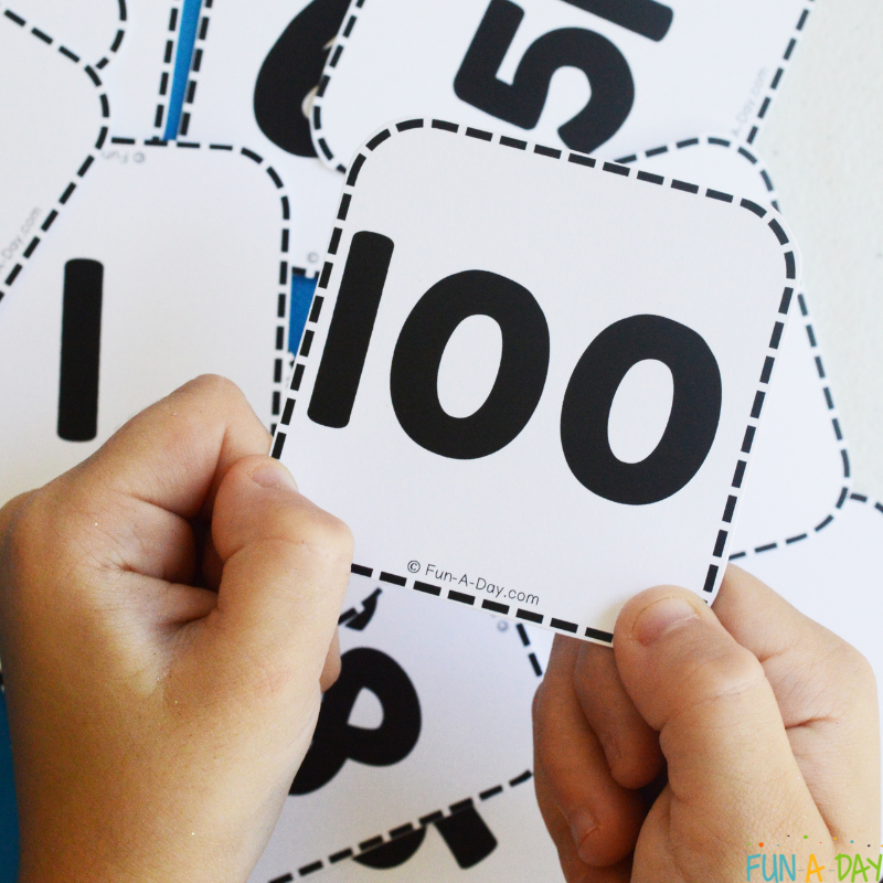 child holding number 100 card over pile of free printable numbers in disarray