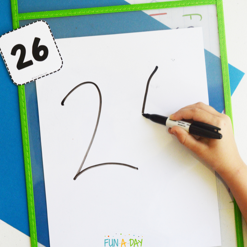 child writing number 26 on white board, using printable number card as reference